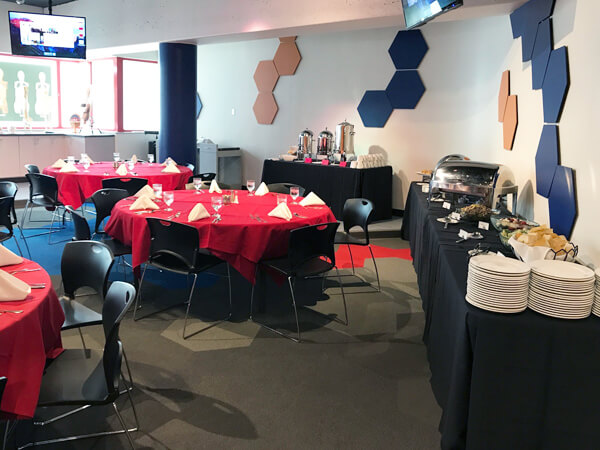 Room filled round tables with red table cloths and black chairs.