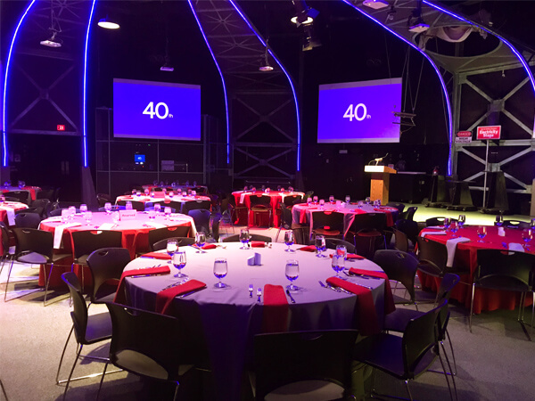 Large room, large monitors and round tables with white table cloths