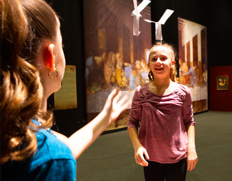 Two girls playing with a paper helicopter in the air.