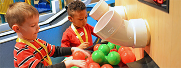 Boys playing red and green balls using conveyors and vacuum tubes