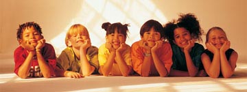 Diverse smiling kids laying on the floor, resting their heads in their hands, looking at camera