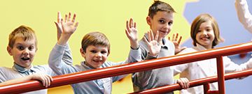 A group of students on a field trip wave excitedly at the camera as they travel between exhibits