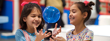 Two girls laugh as they interact with a small floating ball